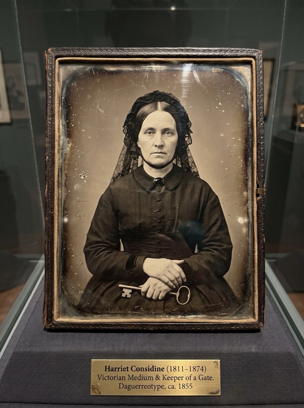 A cased daguerreotype of a seated Victorian woman in mourning dress and lace veil, her hands folded over a large key.